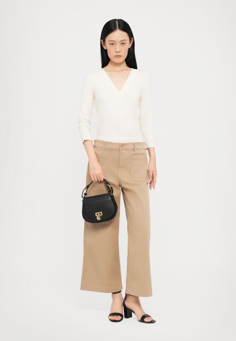 Haut en tricot crème avec un col en V, pantalon beige à jambes larges et sac à main noir. Le mannequin porte des sandales à talons noires, présentant des éléments de design minimalistes.