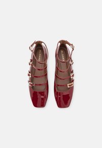 Rote Lackleder-Mary-Jane-Schuhe mit quadrater Spitze, drei Riemen mit goldenen Schnallen und einem glatten Innenfutter.