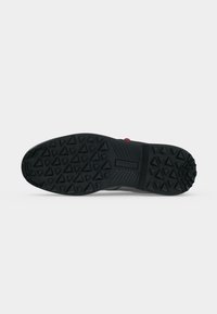 Semelle de chaussure noire avec des motifs de bande de roulement triangulaires profonds et une prise texturée, avec le nom de la marque embossé au centre.