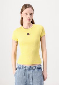 T-shirt jaune à manches courtes côtelé avec un col rond et un petit logo multicolore sur la poitrine. Texture subtile et coupe ajustée.