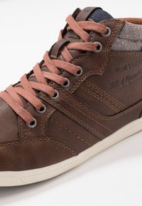 Brązowe skórzane sneakersy z różowymi sznurowadłami, akcent z teksturowanej szarej tkaniny oraz jasnobrązowa gumowa podeszwa. Zawierają logo i szczegóły przeszyć.