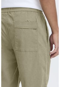 Pantalon cargo vert olive clair doté d'une taille élastique, de deux poches arrière et d'une coupe droite. Texture de tissu textile lisse.