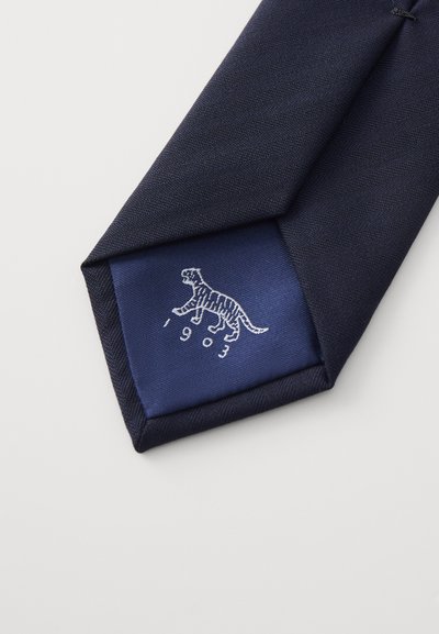 Cravatta blu navy con una texture liscia, presenta una fodera blu a contrasto, che mostra un ricamo di una tigre e l'anno "1903."