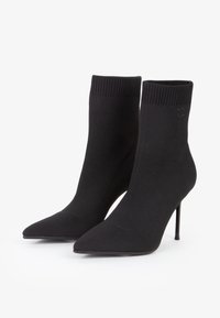 Czarne botki na kostkę wykonane z dzianiny, z prążkowanym mankietem, spiczastym noskiem i smukłym obcasem w kształcie szpilki. Brak widocznych dodatków lub akcentów.