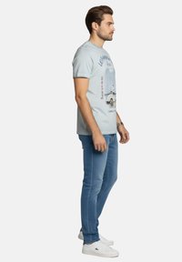 Camiseta de algodón azul claro con un estampado gráfico de un coche. Combinada con vaqueros ajustados de color azul medio y zapatillas blancas.