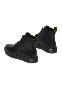Botas de cuero negras hasta el tobillo con puntera redonda, cordones de seis ojales y tirador amarillo texturizado. Presentan una suela negra gruesa y texturizada con costuras amarillas.