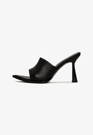 Mules à talons hauts noirs avec un extérieur en cuir lisse, à bout ouvert et au design courbé. Dotés d'un talon aiguille élégant et d'un style minimaliste.