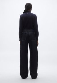 Mornarsko plava pamučna majica dugih rukava s malim gumbom na stražnjoj strani, uparena s tamnoplavim trapericama širokog kroja s džepovima na stražnjoj strani.