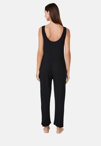 Mono negro acanalado con espalda descubierta y tirantes estilo tank; presenta una silueta ajustada y un diseño de pierna ancha y corta.