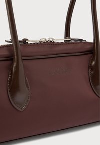 Καφέ τσάντα χειρός με διπλές δερμάτινες λαβές, διπλό ασημί φερμουάρ και ανάγλυφο λογότυπο "LeGer" στο μπροστινό πάνελ.