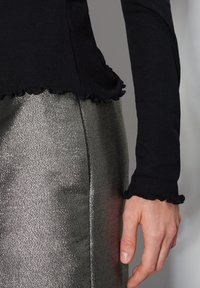 Svart ribbad långärmad topp med volangslung, kombinerad med en glänsande silverkjol som visar upp metallisk textur och en figurnära silhuett.