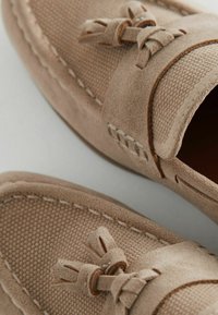 Mocassini beige in tessuto strutturato e morbida suede, con accenti decorativi a nodo sul davanti e cuciture a contrasto.