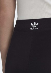 Black athletic leggings featuring a smooth texture and an elastic waistband, with a white Adidas logo prominently displayed at the top.