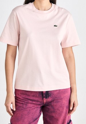 Jasnoróżowy bawełniany t-shirt z krótkimi rękawami i okrągłym dekoltem. Na piersi małe zielone haftowane logo. Prosty krój.