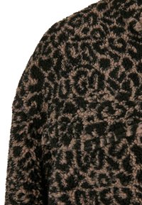 Manteau à motifs noirs et beiges avec un tissu texturé et duveteux arborant un motif floral. La structure est douce et épaisse, idéale pour la chaleur.