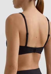 Čierny horný diel bikín s nastaviteľnými ramienkami a zapínaním na háčik vzadu. Tkanina vyzerá hladko s minimom švov.