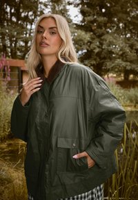 Veste légère vert olive avec un col en velours côtelé, boutons-pression et deux poches latérales. Texture lisse, coupe ample et design décontracté.
