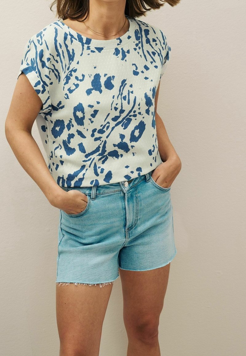 Haut à manches courtes avec un motif abstrait bleu sur un fond clair, associé à un short en denim bleu clair aux bords effilochés.