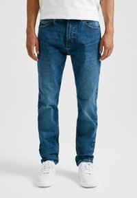 Vaqueros de mezclilla azul claro con corte recto, cinco bolsillos y un desgaste sutil, combinados con zapatillas blancas.