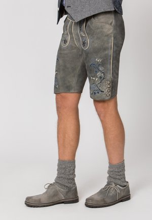 Traditionelle graue Lederhosen-Shorts für Herren mit blauer Blumenstickerei, kombiniert mit grauen Stricksocken und grauen Schnürschuhen.