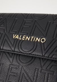 Borsa a mano in pelle nera con logo "VALENTINO" impresso e hardware dorato, texture liscia e design strutturato.