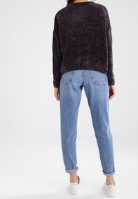 Suéter de textura oscura con un corte holgado, combinado con unos vaqueros tapered en azul claro. Zapatillas blancas completan el look. Puños enrollados visibles.