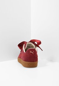 Baskets en velours côtelé rouge avec une semelle en caoutchouc épaisse de couleur marron clair. Elles présentent un grand nœud en satin et un logo Puma au niveau du talon et du côté.