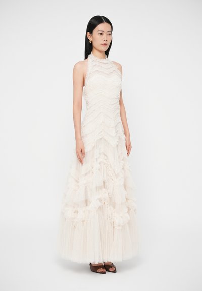 Šaty s halter neck prevedením v svetlej krémovej farbe s vrstvenými volánmi a textúrovanými vrstvami, s dlhou sukňou siahajúcou až na zem a priliehavým živôtikom.