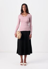 Vaaleanpunainen ribbimäinen pitkähihainen paita, jossa on aaltoileva kaula-aukko, musta pliseerattu midi-hame, beige käsilaukku ja valkoiset korkokengät.