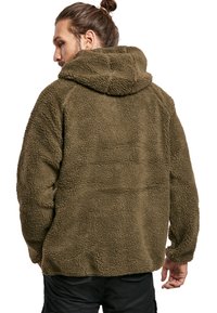 Haut à capuche en polaire vert olive avec une texture pelucheuse, présentant une capuche et une coupe décontractée, avec des coutures visibles aux joints.
