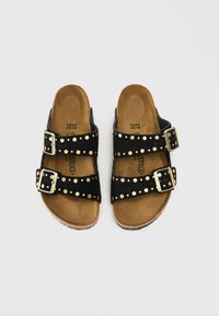 Sandales en suède noir avec deux brides réglables à boucles, ornées d'accents en studs dorés le long des brides et d'une semelle en liège brun.