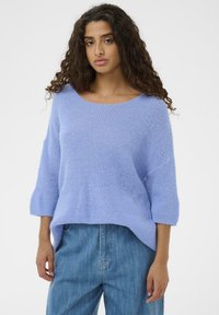 Pull en maille violet clair avec un large col arrondi, des manches trois-quarts et une coupe ample. Associé à un jean en denim bleu.