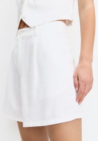 Weiße Leinen-Shorts mit taillierter Passform, ausgestattet mit Seitentaschen und einer glatten Textur. Ein Knopfverschluss rundet das Design ab.