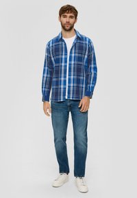 Blauwe geruite overhemden met witte en marineblauwe accenten, gemaakt van katoen, gedragen over een wit T-shirt, gecombineerd met blauwe jeans en witte sneakers.