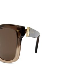 Occhiali da sole con gradiente marrone, grandi lenti quadrate, montatura in plastica liscia e dettagli in metallo dorato sulle tempie.