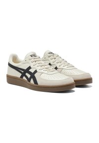 Hvide lædersneakers med sorte detaljer og perforeret tå, udstyret med en brun gummisål og strukturerede snørebånd. Klassisk low-top design.