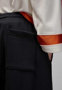 Zwarte joggingbroek met een zijzak, gecombineerd met een wit en oranje gestreept shirt, dat contrasterende kleuren en texturen benadrukt.