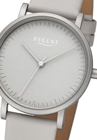 Montre analogique grise avec un cadran lisse, des aiguilles argentées et un design minimaliste. Elle possède un bracelet en cuir gris et un boîtier slim en acier inoxydable argenté.