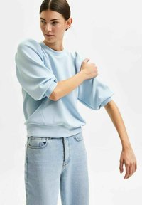 Light blue sweatshirt with puff sleeves and a ribbed hem. Paired with light-washed straight-leg jeans. Soft, smooth fabric texture.