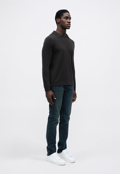 Ciemnoszara dzianinowa polo z długim rękawem, zestawiona z niebieskimi dżinsami i białymi trampkami. Fason jest luźny, z płaskim kołnierzykiem.