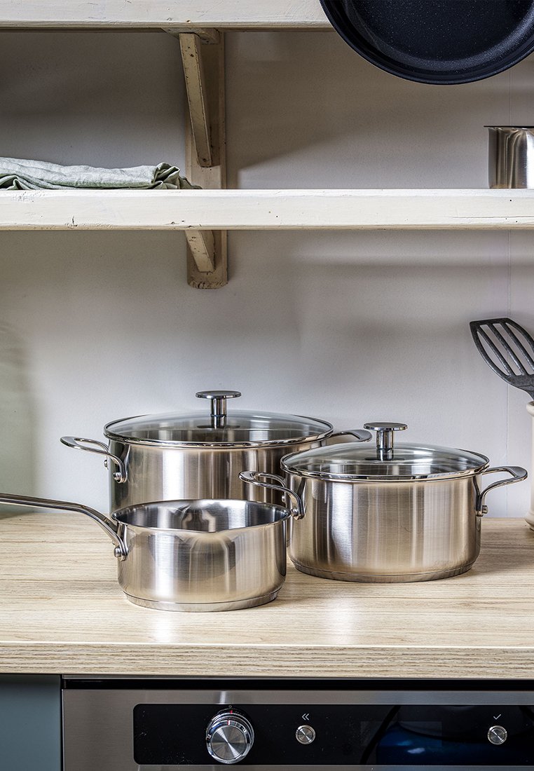 Edelstahl-Kochgeschirrset mit drei Töpfen mit Glasdeckeln, unterschiedlichen Größen, glatter Oberfläche und ergonomischen Griffen auf einer Holzarbeitsplatte.