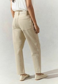 Jean beige taille haute avec une coupe droite, ornés de motifs brodés discrets. Associés à des ballerines texturées de couleur claire.