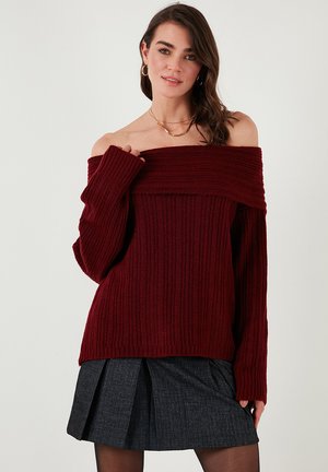 Burgundy ribbed off-the-shoulder sweater with wide sleeves, paired with a pleated gray skirt. Soft texture with a relaxed fit.
