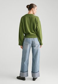 Zielony sweter z dzianiny o luźnym kroju, połączony z jasnoniebieskimi szerokimi spodniami jeansowymi z kontrastowym wykończeniem u dołu i detalem kieszeni z tyłu.