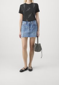 Zwart T-shirt met zilveren bliksemprint, lichtblauwe denim minirok met rafelrand, zwarte gestudde flats en een gebloemde bucketbag.