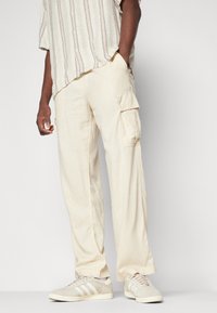 Beige cargobroek gemaakt van lichtgewicht stof met zijzakken, gecombineerd met lichtgekleurde sneakers. Het shirt heeft een gestreept patroon in neutrale tinten.