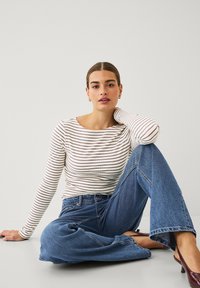 Haut à rayures blanches et marron à manches longues associé à un jean en denim bleu à jambes larges. La tenue présente une coupe décontractée et une texture douce.