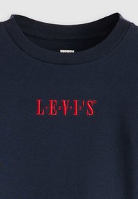 Modra bombažna majica s kratkimi rokavi, ki ima okrogel izrez in rdečo vezeno oznako "LEVI'S" z izpostavljenim besedilom.