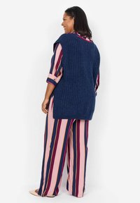 Chaleco de punto acanalado en navy sobre una camiseta de manga larga a rayas multicolores en rosa, marrón y navy, y pantalones de pierna ancha a juego; tejido suave, corte relajado.