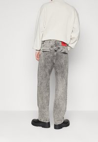 Harmaat happopesulla pestyt farkut, väljät, takana punainen merkki, mustat massiiviset kengät ja off-white-ylimitoitettu paita.